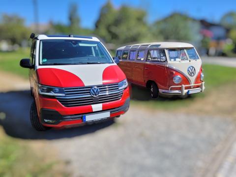 Neues Modell oder Vorgänger? Unterschiede erkennen und richtig entscheiden – mit Autochampion24 Zwei VW Bullis in identischem Rot-Weiß-Design: Ein moderner VW T6 und ein klassischer VW T1 Bus nebeneinander im Freien – Symbol für den Generationenwechsel.